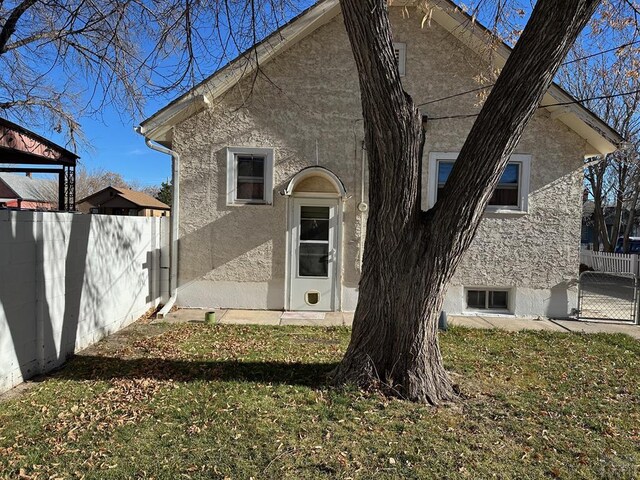 rear view of property featuring a yard, fence, and stucco siding