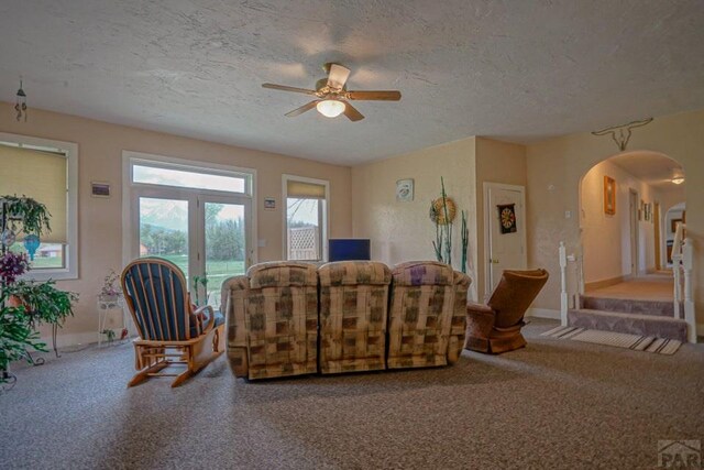 carpeted living area with a ceiling fan, arched walkways, and a textured ceiling