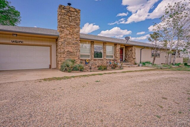 ranch-style house featuring an attached garage, stone siding, dirt driveway, and a chimney