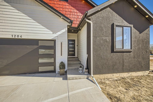 doorway to property with a garage, concrete driveway, and stucco siding