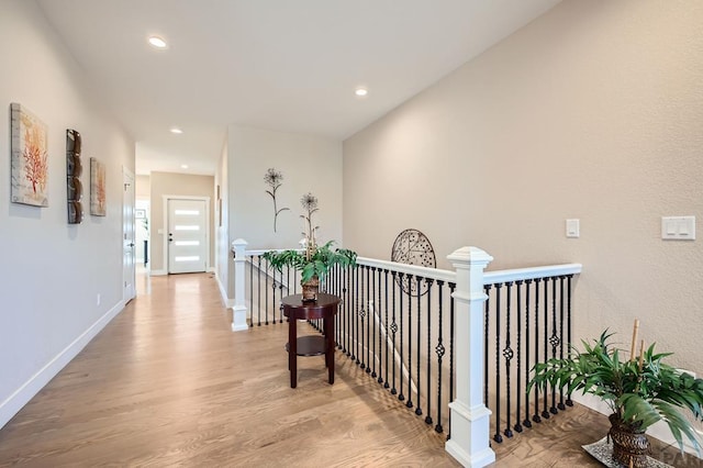 corridor with baseboards, light wood-style flooring, an upstairs landing, and recessed lighting