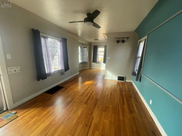 unfurnished living room with ceiling fan, light wood finished floors, visible vents, and baseboards