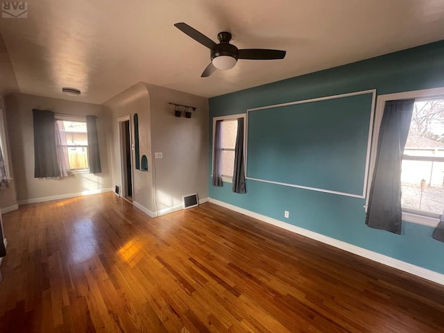 empty room with ceiling fan, wood finished floors, visible vents, and baseboards