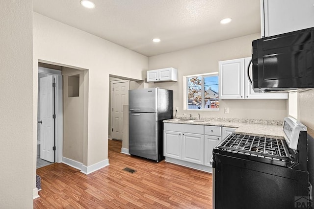 kitchen with black microwave, visible vents, white cabinets, freestanding refrigerator, and gas range oven