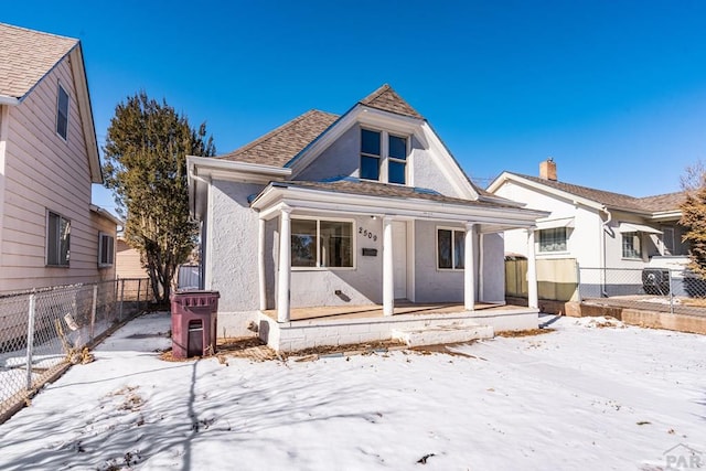 snow covered back of property with fence private yard, covered porch, roof with shingles, and stucco siding