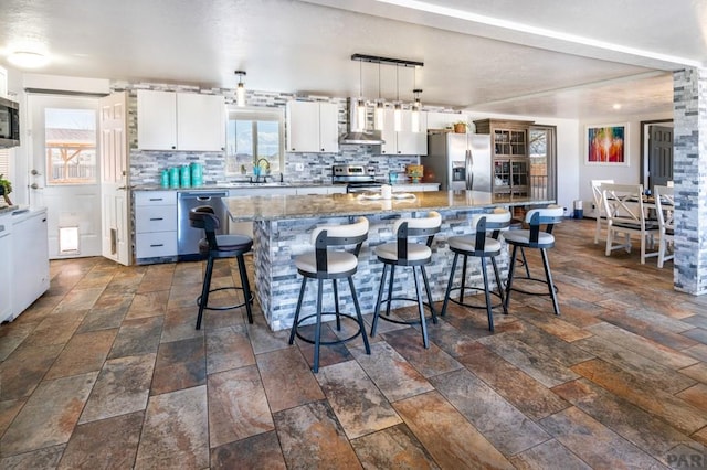 kitchen featuring a large island, stone tile flooring, stainless steel appliances, backsplash, and wall chimney exhaust hood