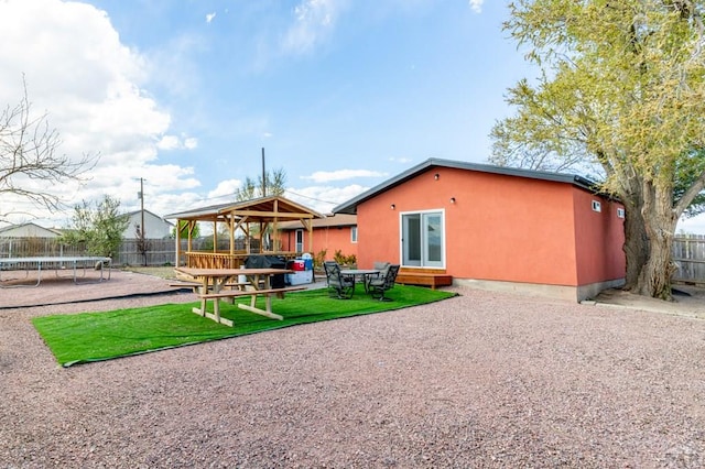 back of property with a gazebo, a trampoline, fence, a yard, and a patio