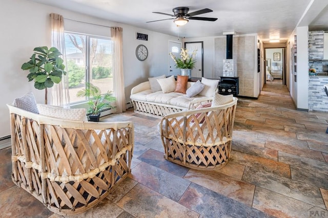 living room featuring stone tile floors, ceiling fan, a baseboard radiator, and a wood stove