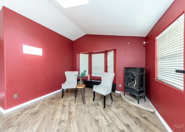 sitting room with baseboards, vaulted ceiling, a wealth of natural light, light wood finished floors, and a wood stove