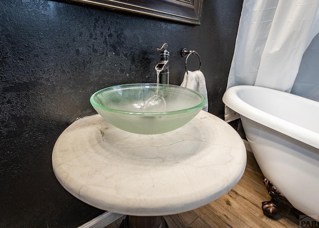 bathroom featuring wood finished floors, a textured wall, a freestanding tub, and a sink