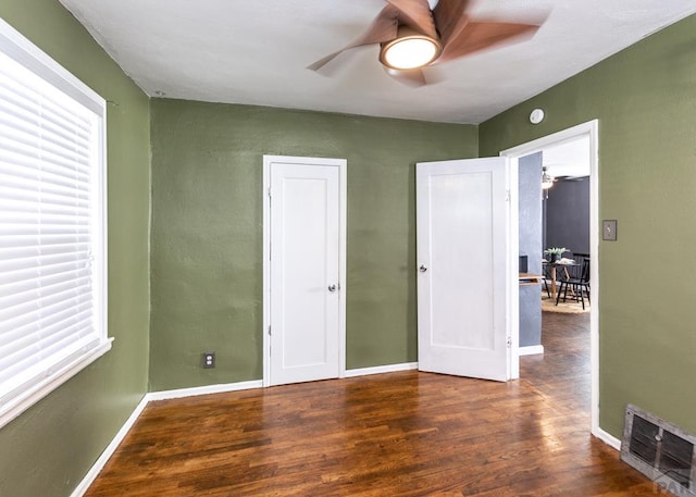 unfurnished bedroom with dark wood-style floors, visible vents, baseboards, and multiple windows