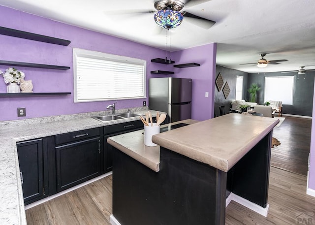 kitchen featuring a sink, a kitchen island, light countertops, freestanding refrigerator, and light wood finished floors