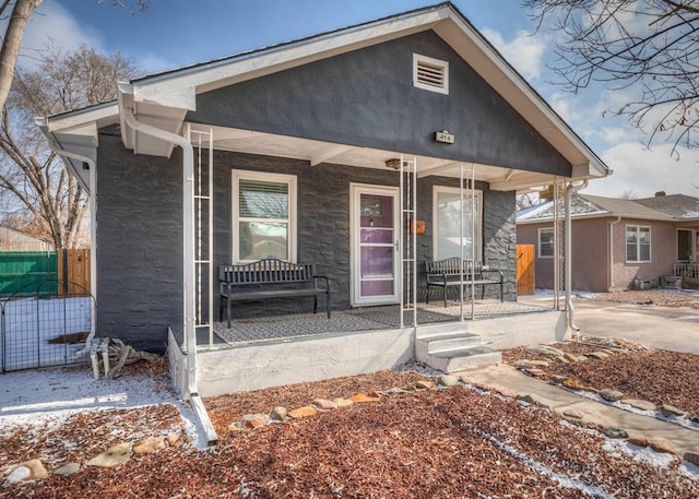 bungalow featuring covered porch, fence, and stucco siding