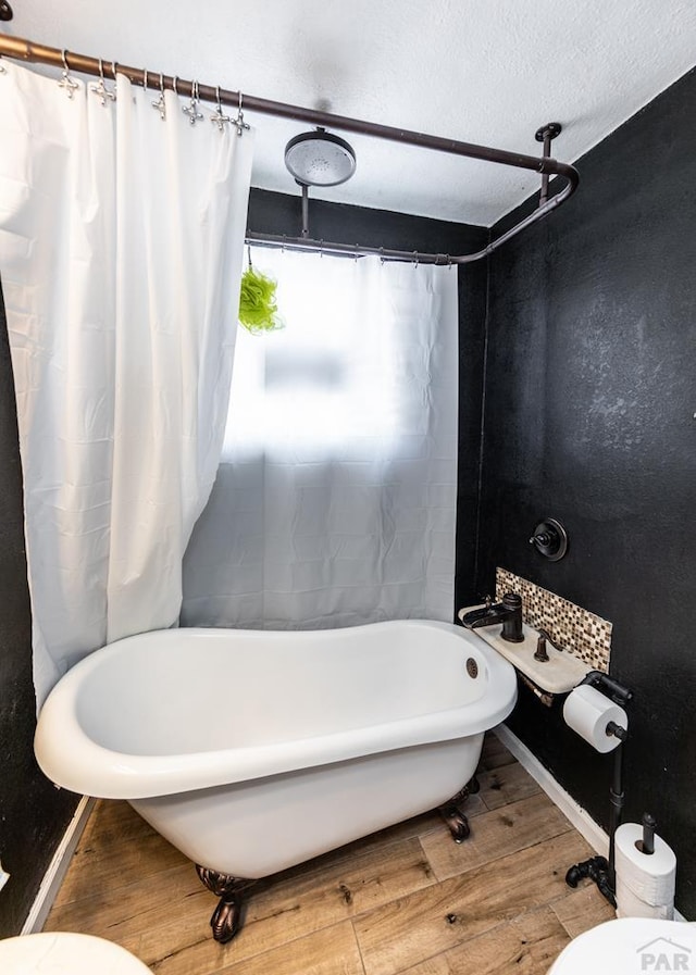 bathroom with baseboards, toilet, wood finished floors, a textured ceiling, and a freestanding tub