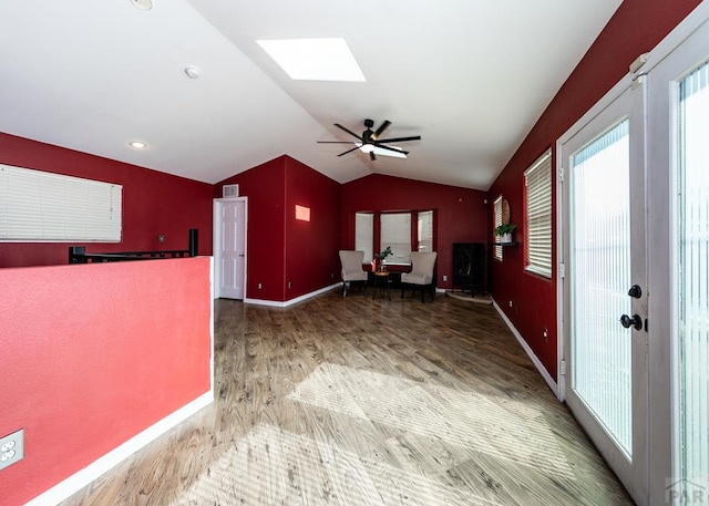 unfurnished room with a ceiling fan, vaulted ceiling with skylight, baseboards, and wood finished floors