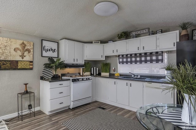 kitchen with dark countertops, white appliances, white cabinetry, and lofted ceiling