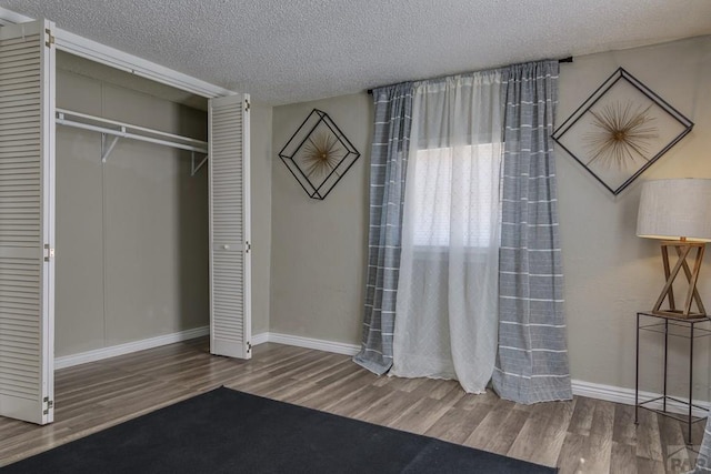 unfurnished bedroom with a textured ceiling, a closet, wood finished floors, and baseboards