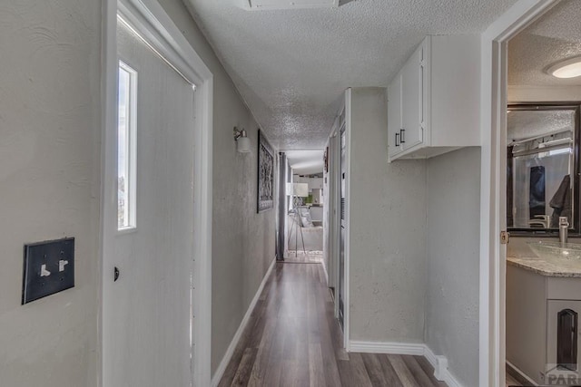 hall featuring a textured ceiling, baseboards, and wood finished floors