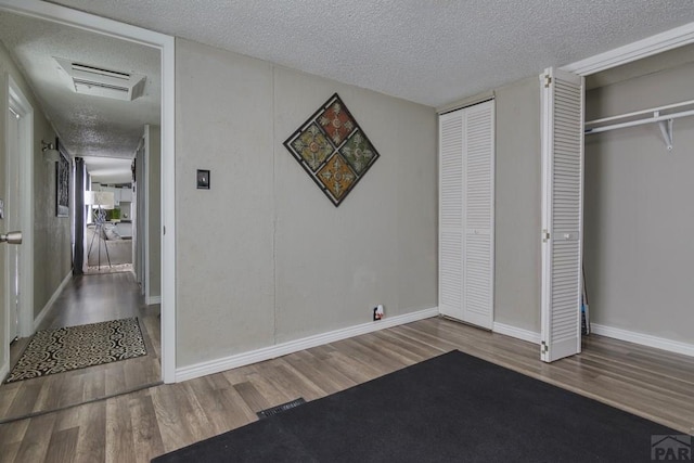 unfurnished bedroom with baseboards, visible vents, wood finished floors, a textured ceiling, and multiple closets