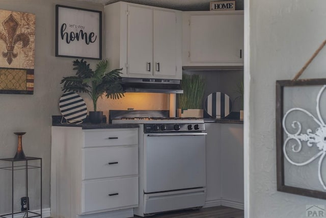 kitchen featuring dark countertops, under cabinet range hood, white gas range oven, and white cabinets