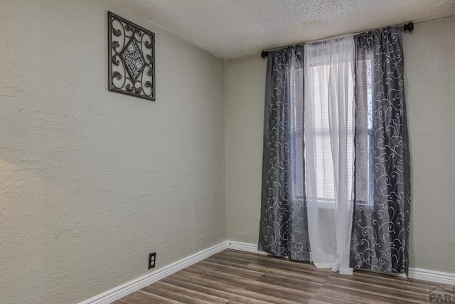 spare room featuring a healthy amount of sunlight, a textured ceiling, baseboards, and wood finished floors