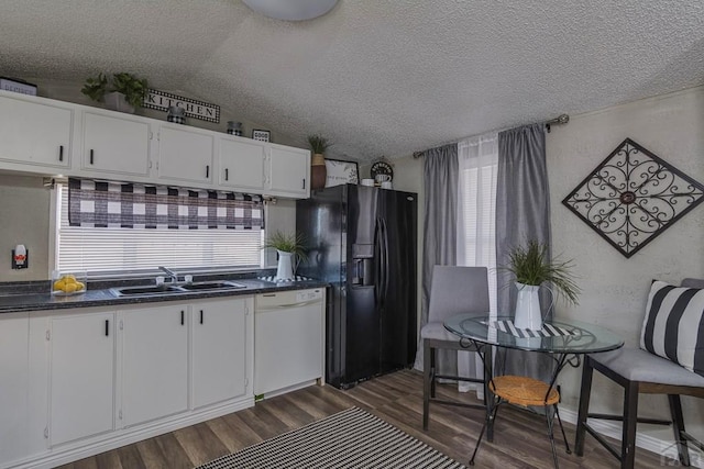 kitchen with dark countertops, white cabinets, a sink, dishwasher, and black fridge