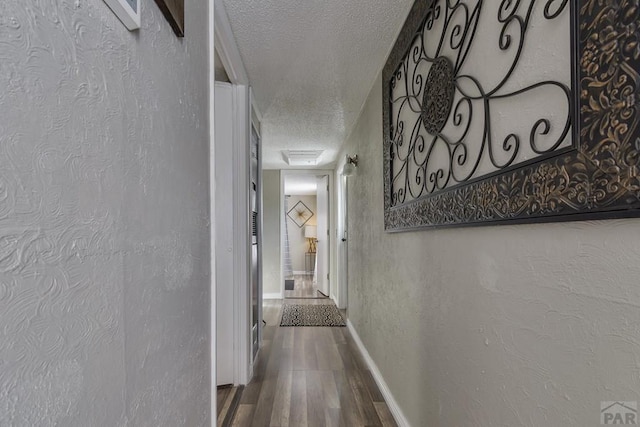 corridor with a textured wall, a textured ceiling, baseboards, and wood finished floors