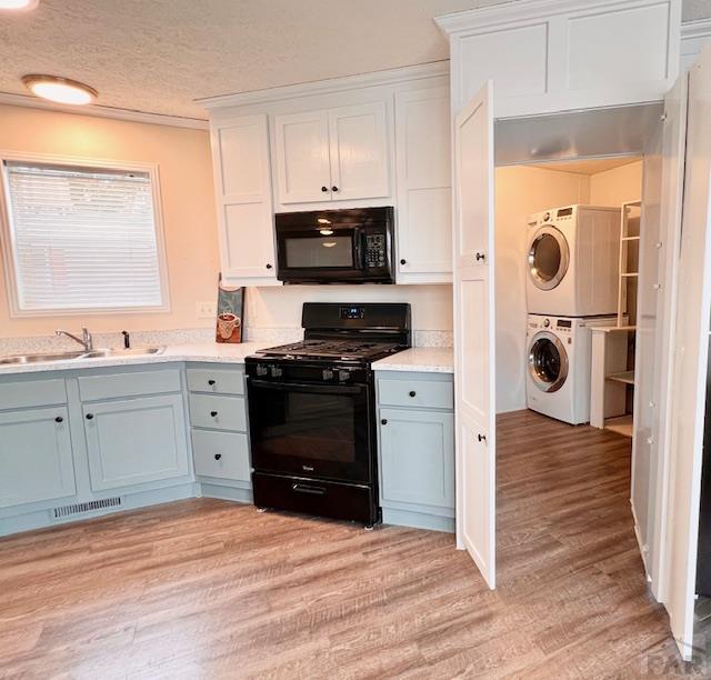 kitchen featuring visible vents, a sink, black appliances, light wood-style floors, and stacked washer / drying machine