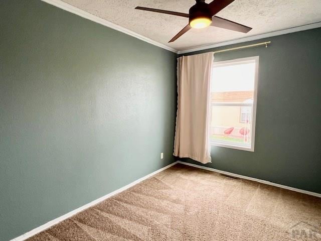 carpeted empty room with a textured ceiling, a ceiling fan, baseboards, and ornamental molding