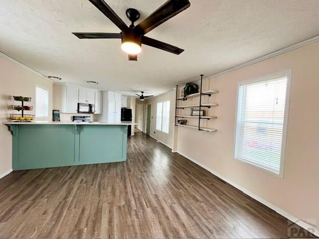 kitchen featuring a ceiling fan, a peninsula, dark wood-style flooring, a textured ceiling, and stainless steel microwave