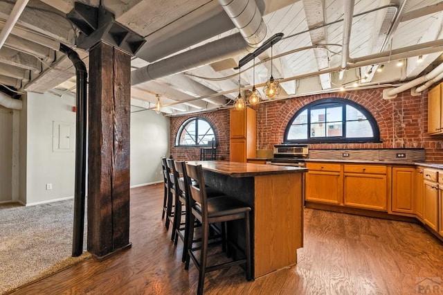 201 Lamkin Unit 205, Pueblo, CO 81003 - kitchen with dark wood-type flooring, a kitchen bar, a kitchen island, brick wall, and dark countertops