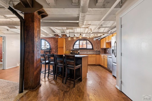 201 Lamkin Unit 205, Pueblo, CO 81003 - kitchen featuring light wood-type flooring, brick wall, stainless steel fridge, light brown cabinetry, and a breakfast bar area