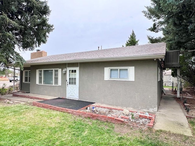 rear view of property featuring roof with shingles, a chimney, a lawn, and stucco siding