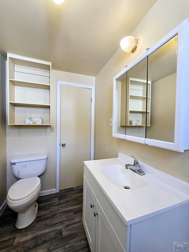 half bathroom with vanity, wood finished floors, toilet, and baseboards