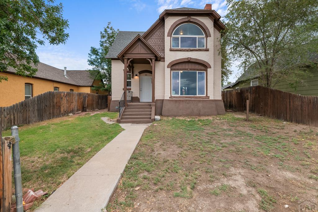 607 W 12th St, Pueblo, CO 81003 - traditional home featuring a chimney, fence, a front lawn, and brick siding
