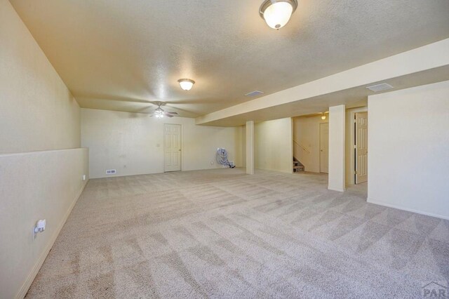 finished basement with light carpet, a textured ceiling, stairs, and visible vents