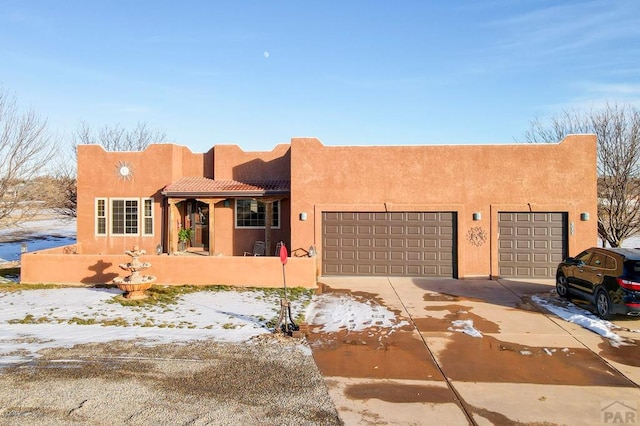 pueblo revival-style home featuring a garage, concrete driveway, and stucco siding