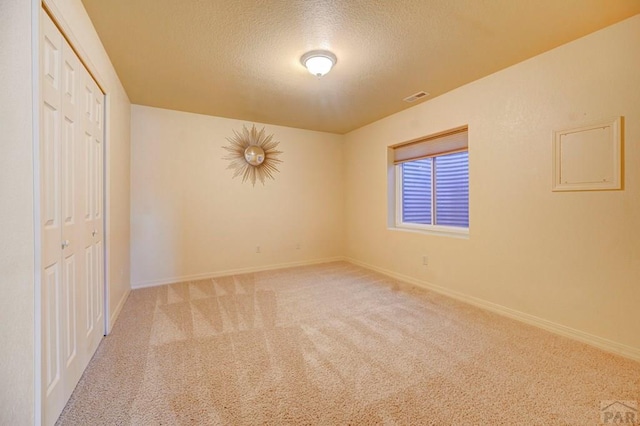 spare room featuring light carpet, a textured ceiling, visible vents, and baseboards