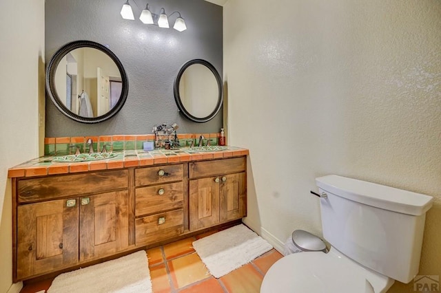 bathroom with double vanity, tile patterned flooring, a sink, and toilet