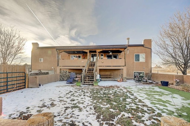 snow covered property featuring stairway, fence, and stucco siding