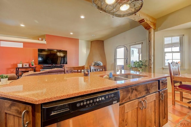 kitchen featuring brown cabinetry, open floor plan, a kitchen island with sink, a sink, and dishwasher