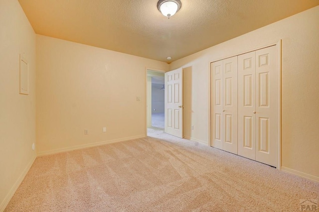 unfurnished bedroom featuring a closet, light colored carpet, a textured ceiling, and baseboards