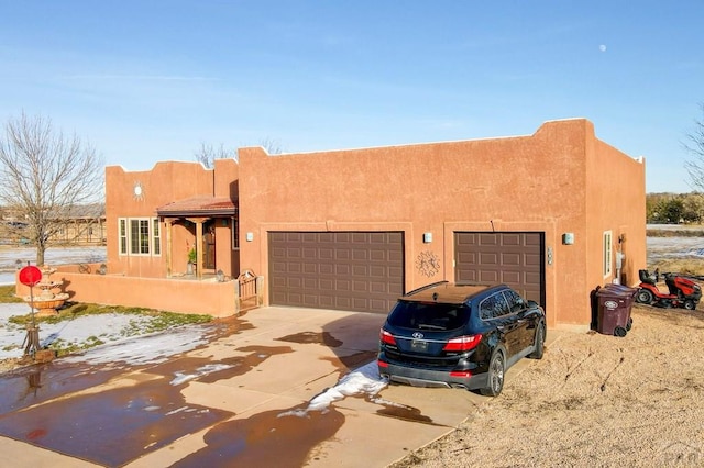 pueblo revival-style home with driveway, an attached garage, and stucco siding