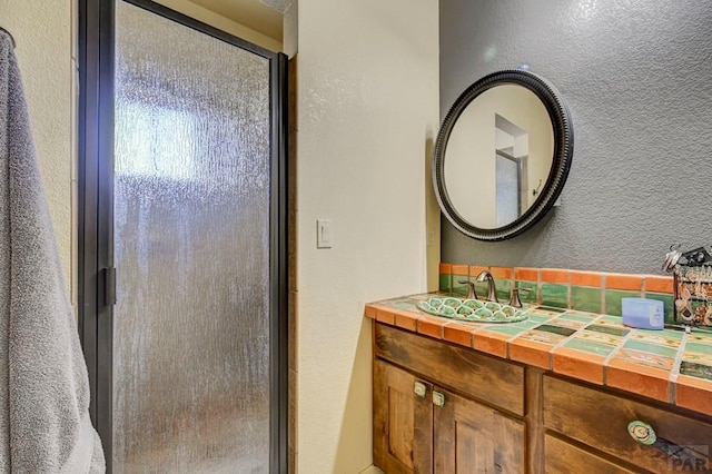 full bath featuring a textured wall, vanity, and a shower with shower door