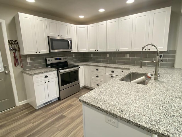 kitchen with a sink, white cabinets, light stone countertops, and stainless steel appliances
