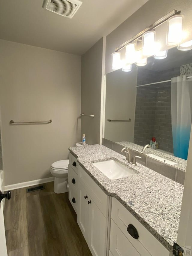 full bathroom with visible vents, a tile shower, wood finished floors, vanity, and toilet