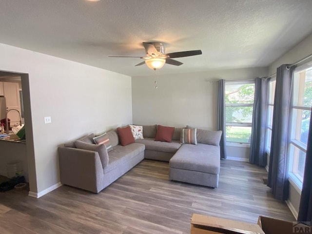 living area with baseboards, a ceiling fan, a textured ceiling, and wood finished floors