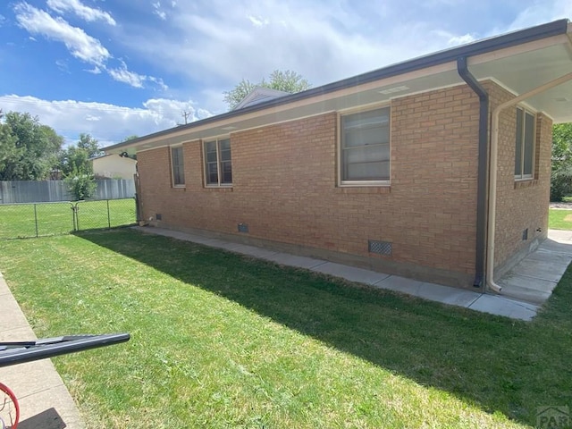 view of side of property with a yard, crawl space, fence, and brick siding