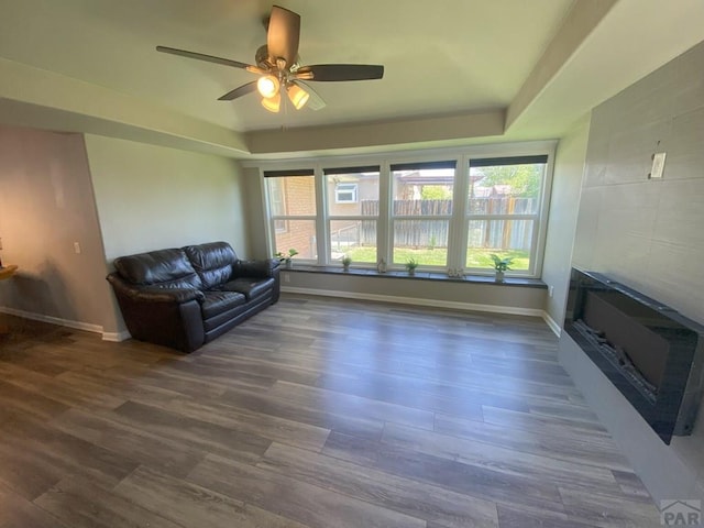 living room with a tray ceiling, baseboards, a ceiling fan, and dark wood-style floors