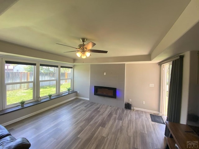 unfurnished living room featuring a large fireplace, baseboards, a ceiling fan, and wood finished floors
